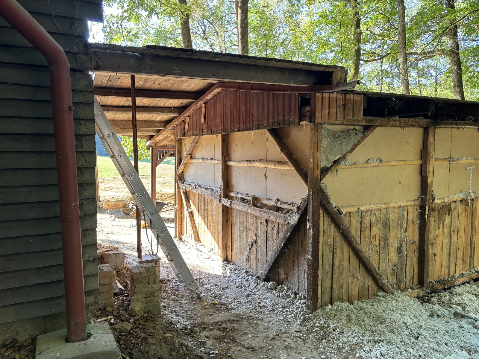Odkrytá stěna chatky se starou izolací pod okrajem lesa